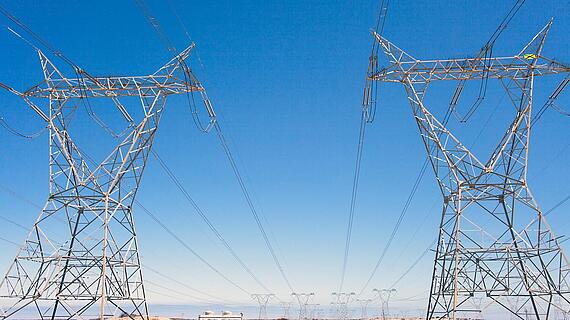 Zwei hohe Strommasten auf freiem Feld mit verlaufenden Hochspannungsleitungen vor blauem Himmel. Energieversorgung in der Nähe von Kapstadt