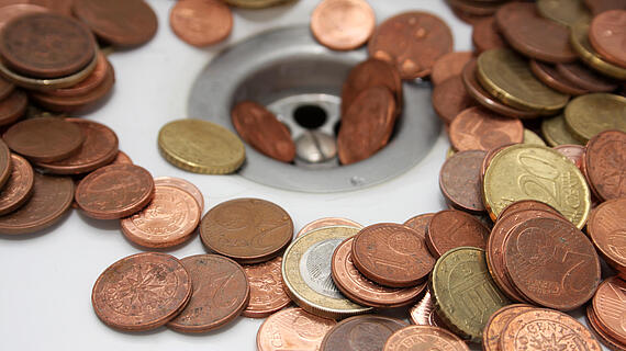 Eine Ansammlung von verschiedenen Euro- und Cent-Münzen liegt rund um einen Abfluss. 