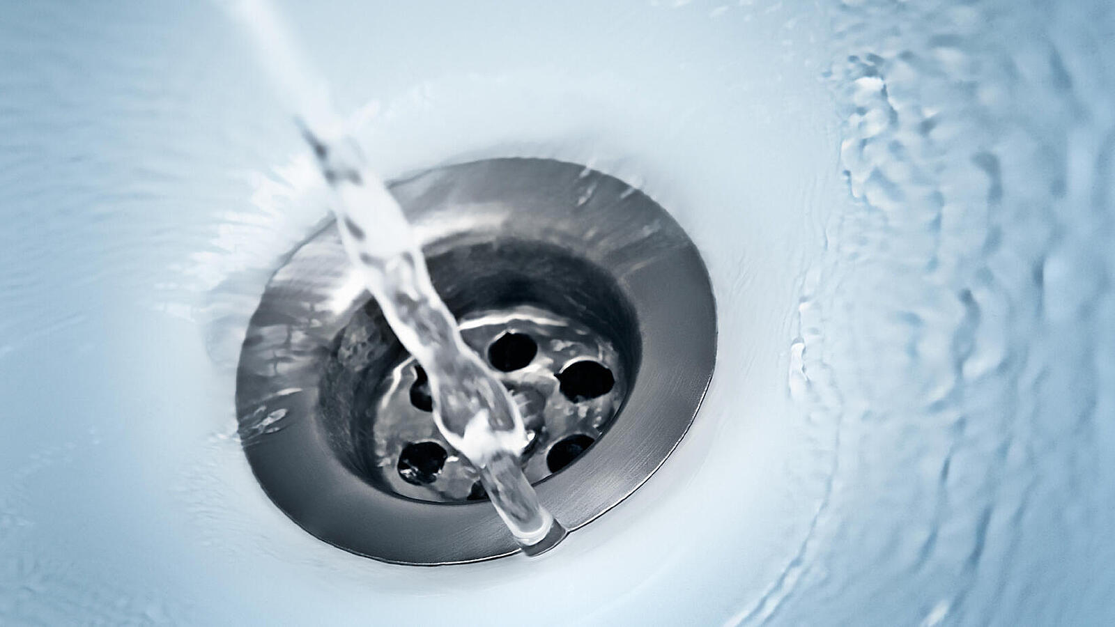 Wasser läuft in ein Waschbecken. Man schaut von oben auf den Abfluss. 