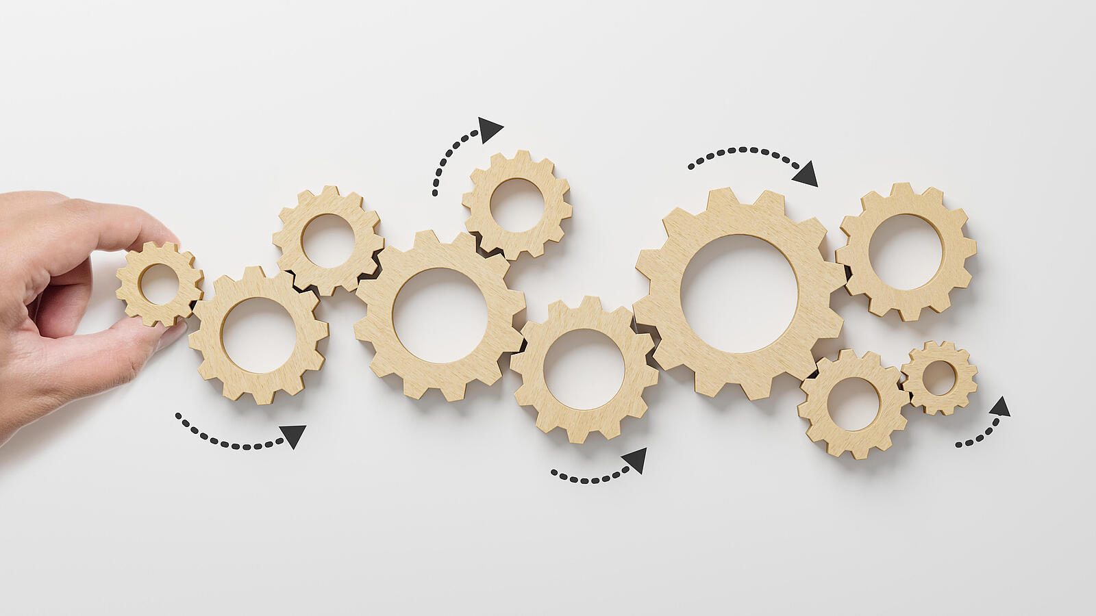 Zahnräder aus Holz in verschiedenen Größen liegen aneinander. Eine Hand hält ein Zahnrad zwischen Zeigefinger und Daumen.