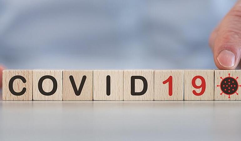 Hand zeigt auf Holzwürfel mit der Aufschrift COVID-19