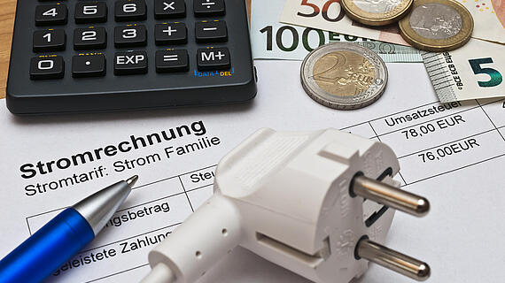Eine Stromrechnung mit dem Titel "Stromtarif: Strom Familie" liegt auf einem Tisch. Neben der Rechnung befindet sich ein weißer Stecker, ein blauer Kugelschreiber, eine Zahlsumme von 78,00 EUR sowie eine Kalkulationsmaschine und verschiedene Euro-Münzen.