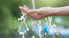Water pouring in woman hand on nature background, environment issues