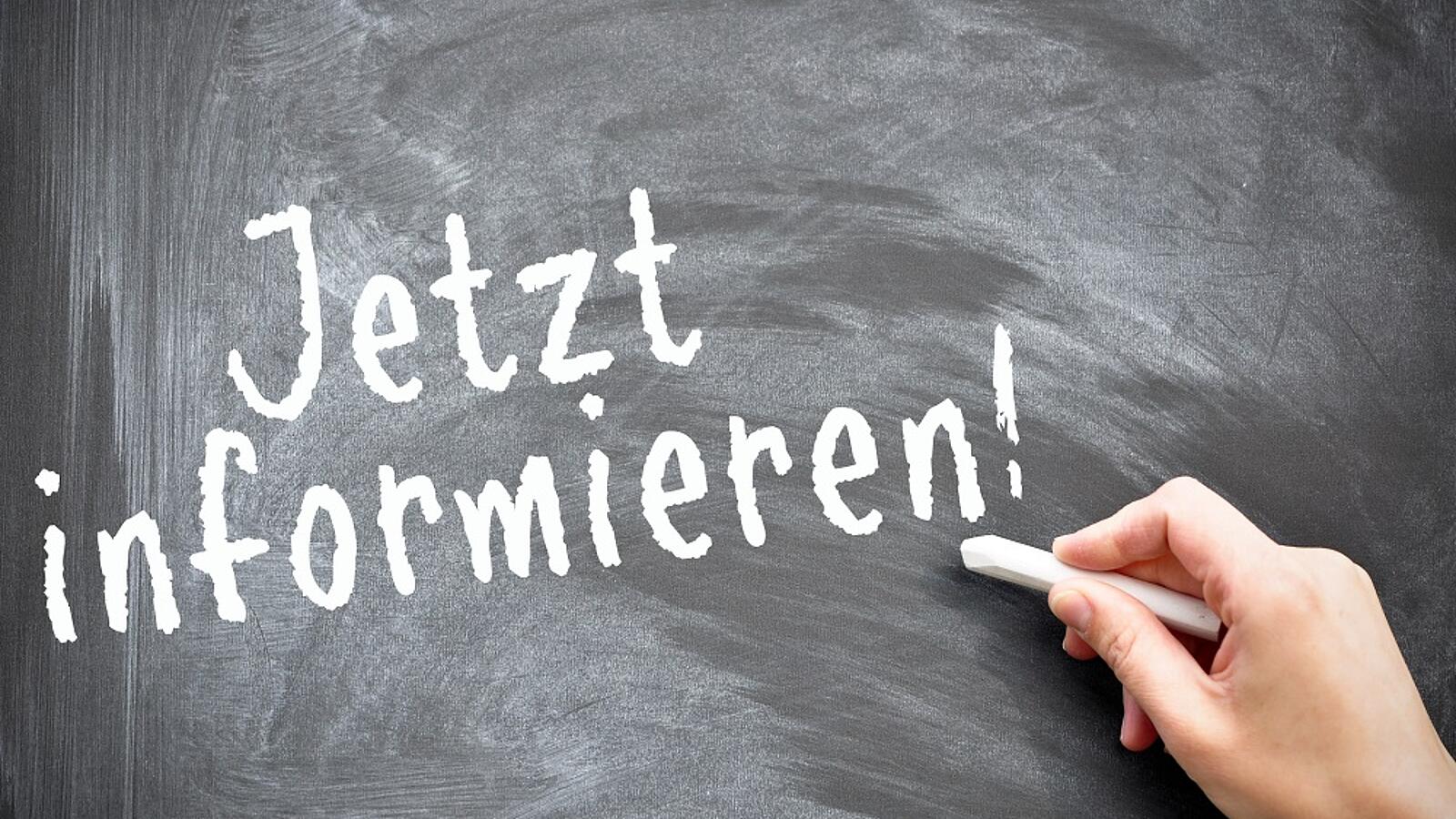 Eine Hand hält weiße Kreide an eine schwarze Tafel, auf der steht 'Jetzt informieren!'