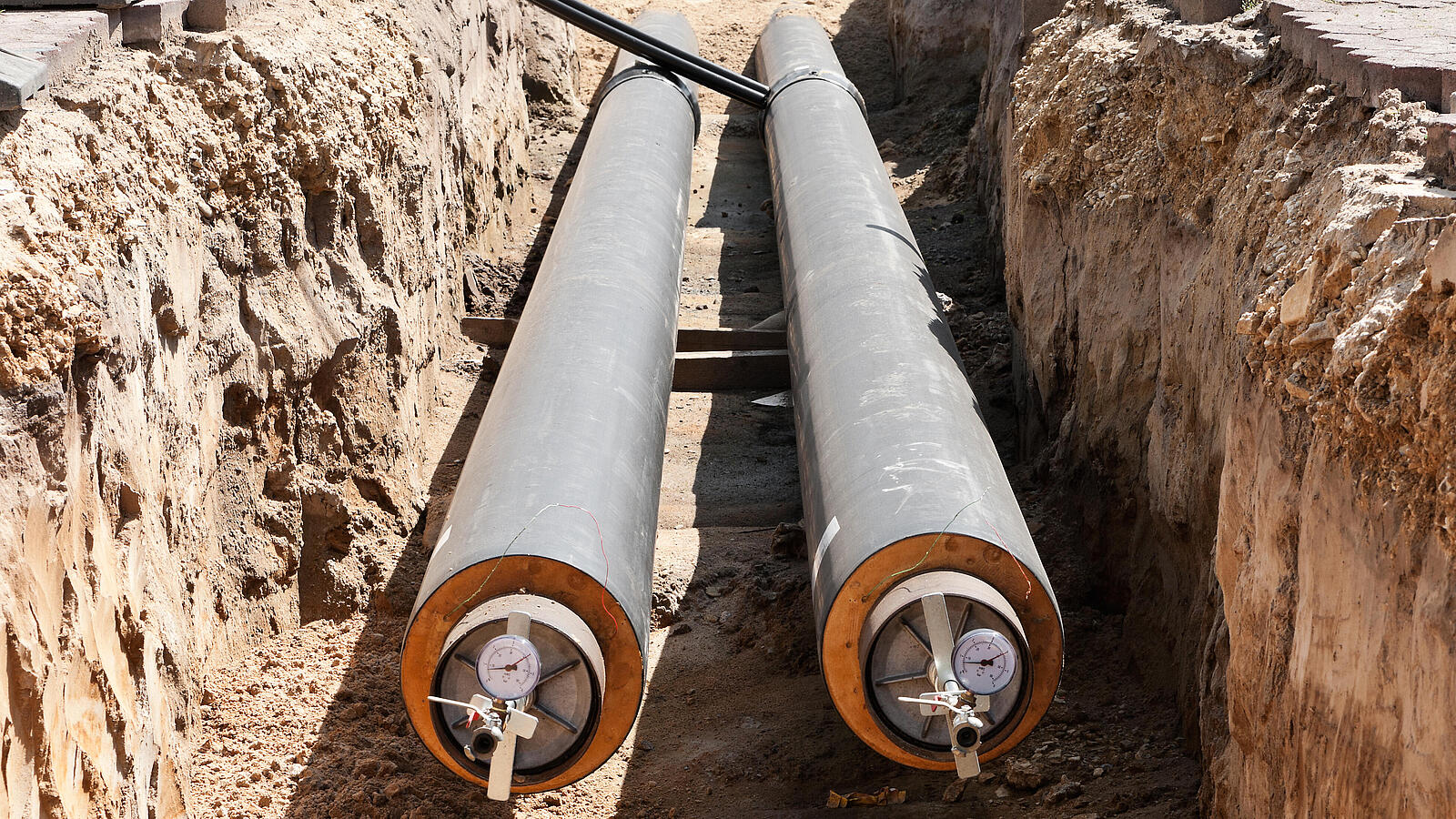 Zwei Rohre liegen in einem ausgegrabenem Schacht aus Erde und Steinen