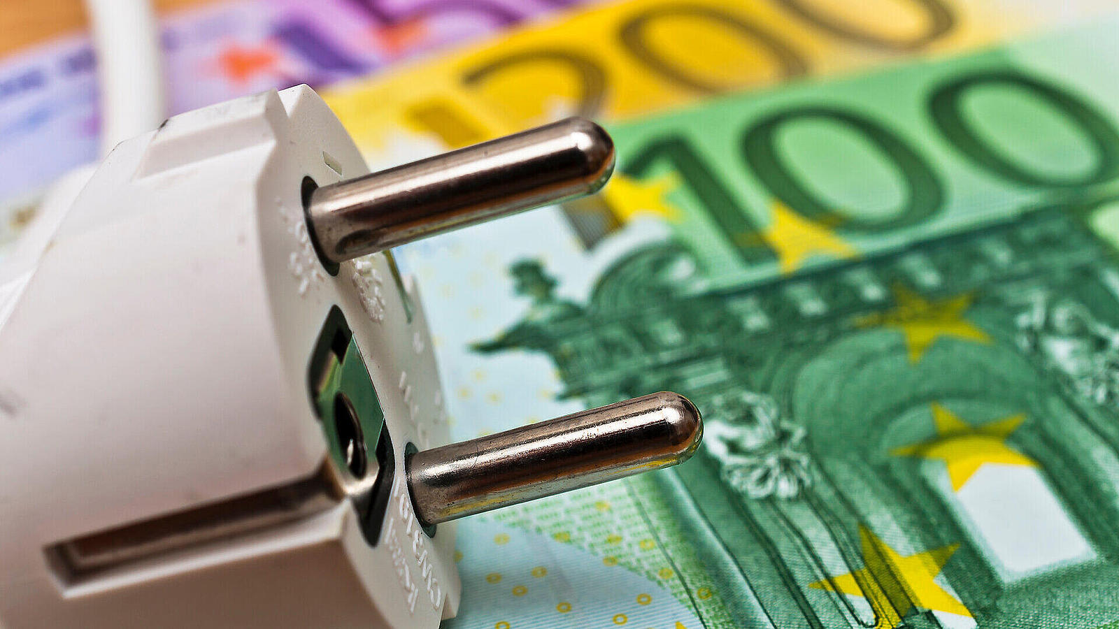 Ein weißer europäischer Netzstecker liegt auf Euro-Banknoten, darunter 500-, 200- und 100-Scheine im Nahaufnahme.