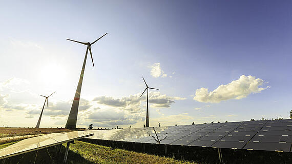 Windkraftanlagen neben einer Solaranlage in einer offenen Landschaft unter einem klaren Himmel mit einigen Wolken.