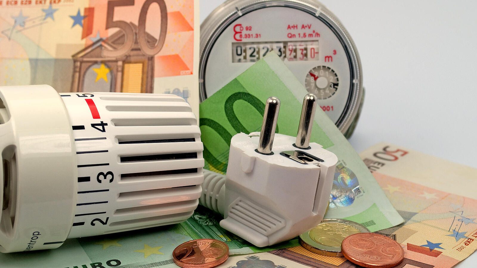 Ein Thermostatkopf, ein Stecker und ein Stromzähler liegen beieinander. Dazwischen liegen Euroscheine und Centmünzen