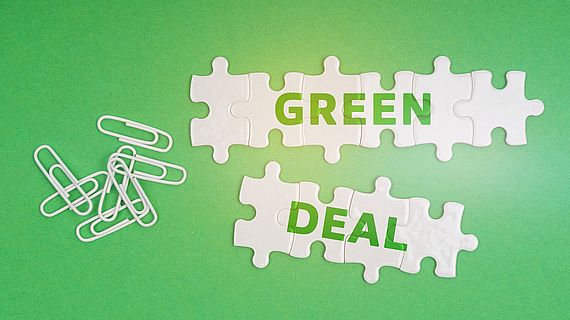 On a green background, paper clips and white puzzles with the inscription - Green Deal