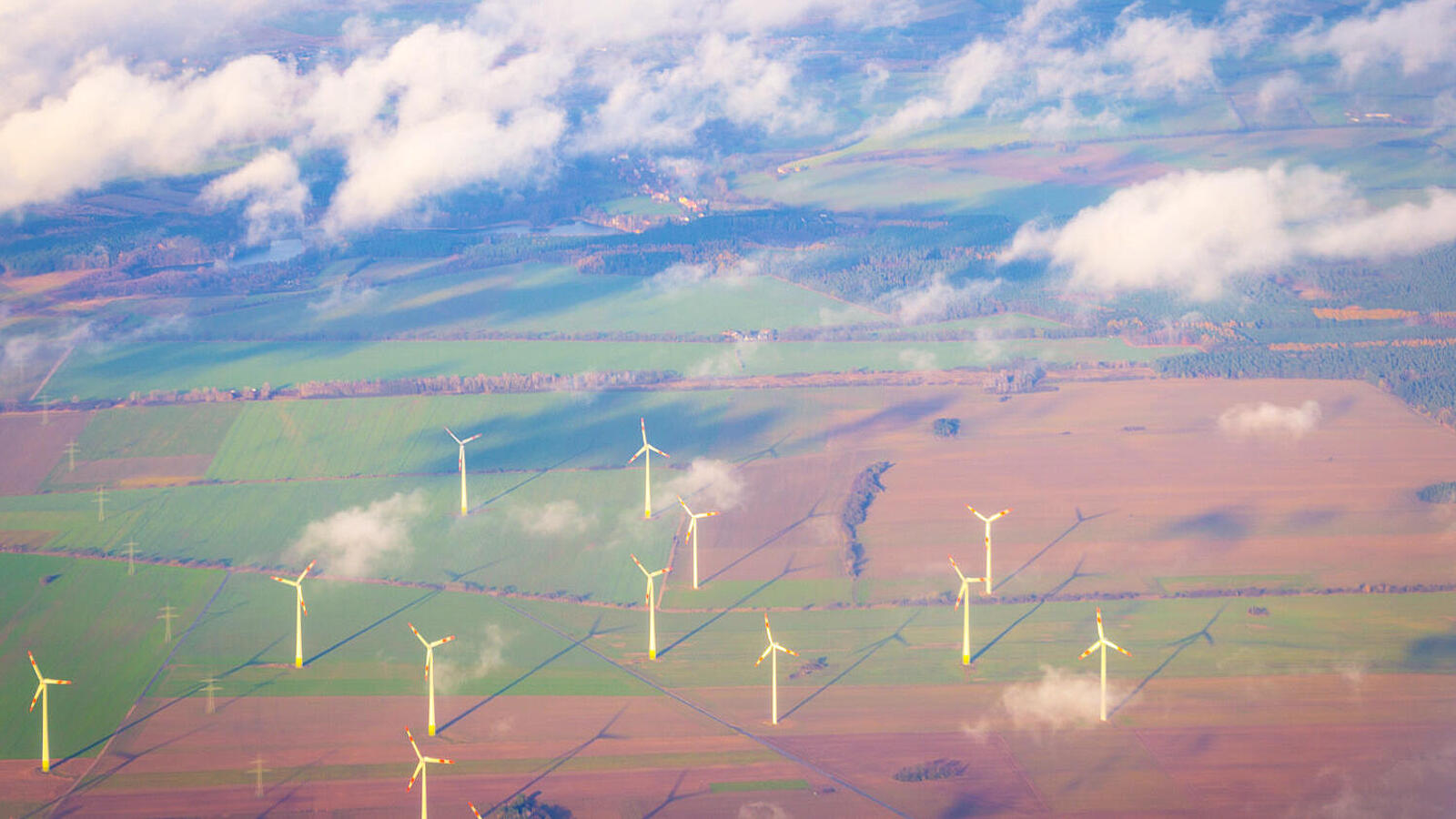 Luftaufnahme von Feldern mit mehreren Windkraftanlagen unter blauem Himmel und vereinzelten Wolken.