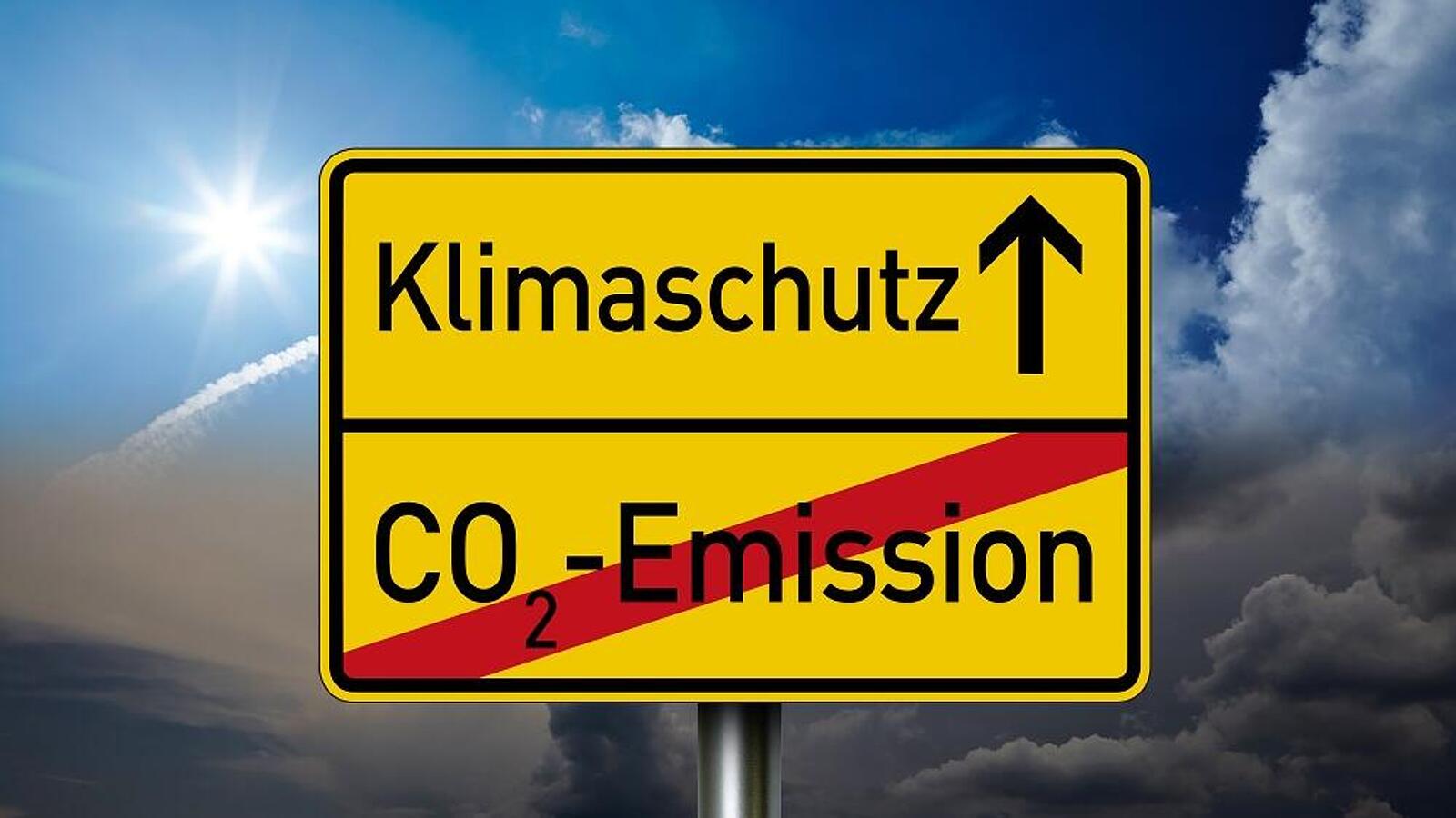 Ein gelbes Ortsschild, auf dem Klimaschutz steht mit einem Pfeil nach oben. Darunter ist mit roter Linie 'CO2-Emission' durchgestrichen.