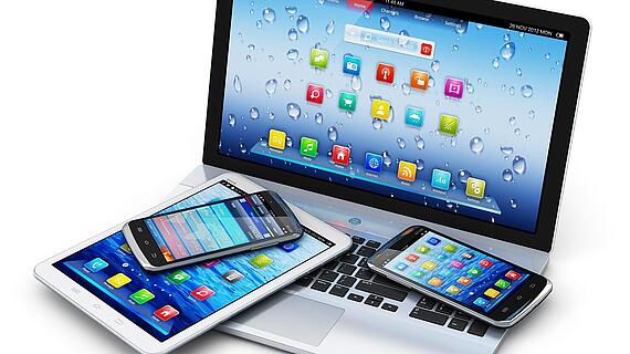 Auf einem Laptop liegen zwei Smartphones und ein Tablet