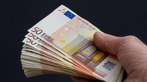 Eine Hand hält mehrere 50-Euro-Scheine, die übereinander gestapelt sind. Der Hintergrund ist schwarz, was den Fokus auf das Geld legt.