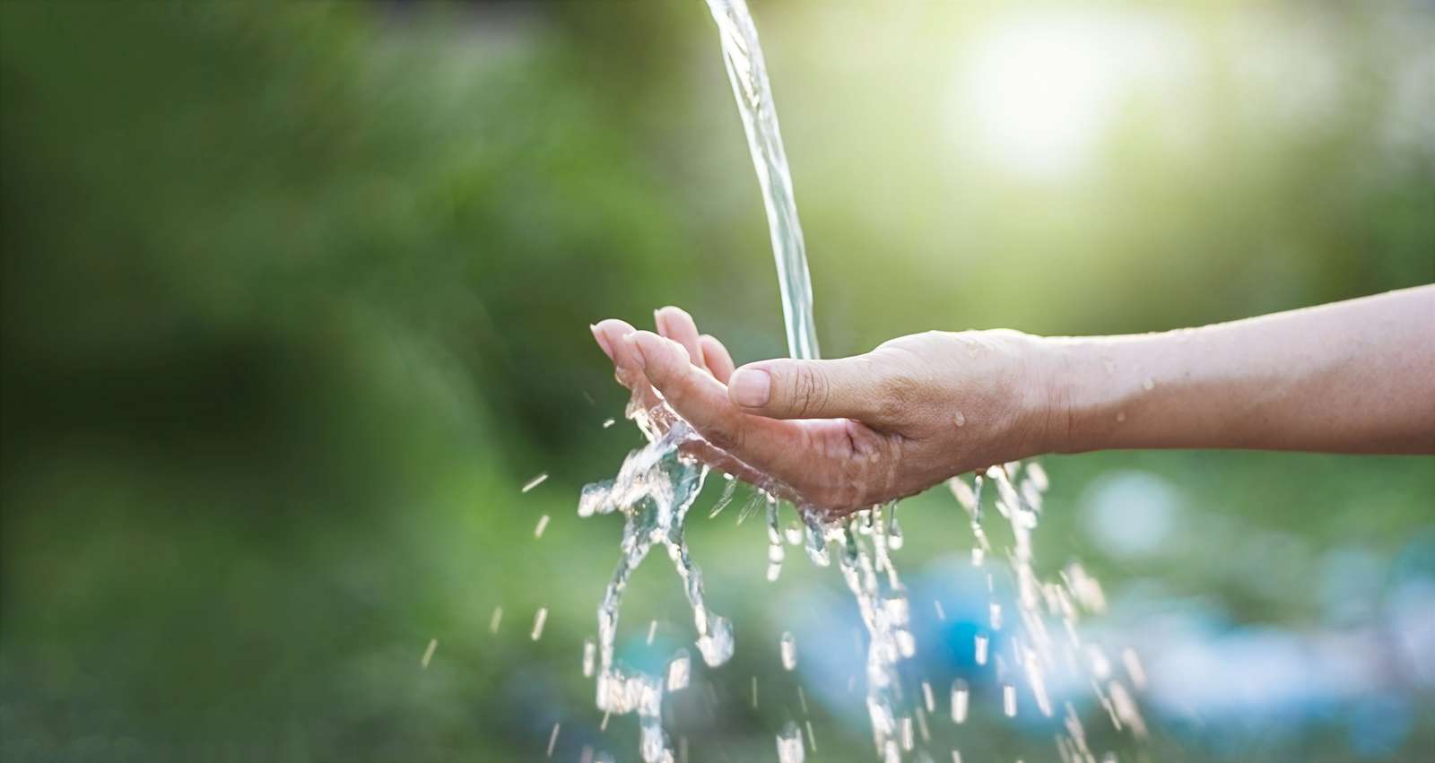 Wasser fließt aus einem Hahn in die Hand einer Frau vor grünem Hintergrund.